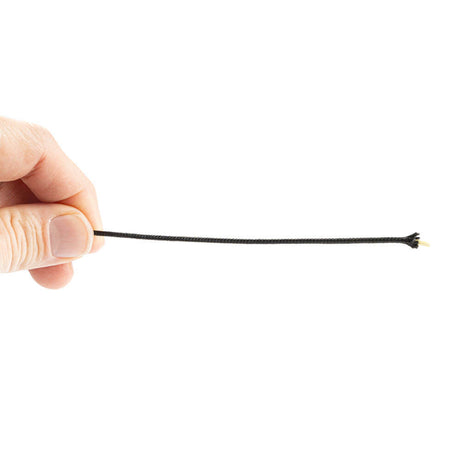 A hand holds a thin, black Kevlar aramid fiber with a polyester sheath. The fiber is taut, with a small, yellow core visible through the black sheath at one end. The background is completely white.